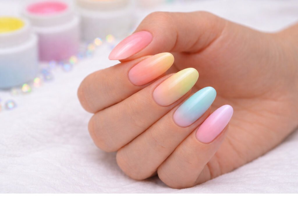 Main féminine avec vernis semi-permanent en dégradé pastel coloré, style baby-color, sur fond neutre beige.